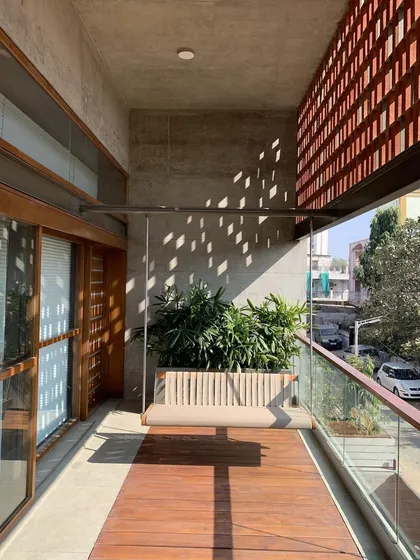 This balcony features a beautiful wooden deck and a hanging swing, with a terracotta jali wall that provides privacy while allowing for airflow and interesting light patterns.
