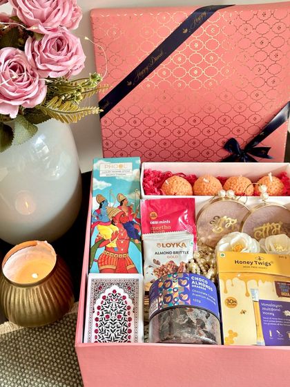A beautiful Moroccan-print pink box sets the stage for this delightful Diwali hamper. Inside, you'll find Phool incense sticks, playing cards, almond brittle, ladoo candles, and other festive goodies, perfect for sharing with loved ones.