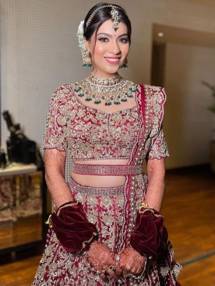 A happy bride in a deep red lehenga, her hair styled in a neat bun with white flowers.