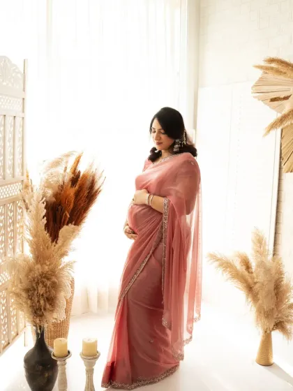 A full-length shot of a mother-to-be in a stunning pink saree, standing in our bright, bohemian-themed studio. A perfect blend of tradition and modern style.