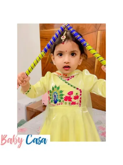 Ready for dandiya night. This little girl is all set for Navratri in her yellow Anarkali-style dress with peacock embroidery, holding her dandiya sticks.