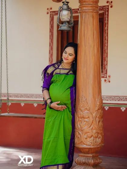 A serene moment captured as the mother-to-be rests against a carved wooden pillar, her hands gently holding her belly.
