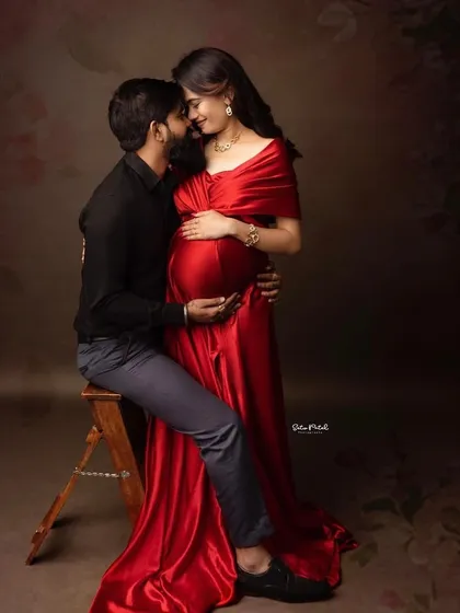 A tender moment with the partner seated. The rich red satin of the Valentina gown drapes beautifully, creating a luxurious and romantic feel.