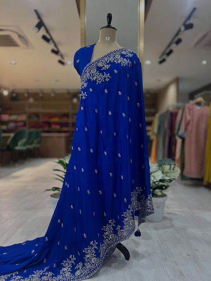 Full-length views of our Chinon party wear sarees, displayed on a mannequin. Available in stunning red and royal blue, these sarees feature intricate scalloped borders and come with a matching pre-stitched embroidered blouse.