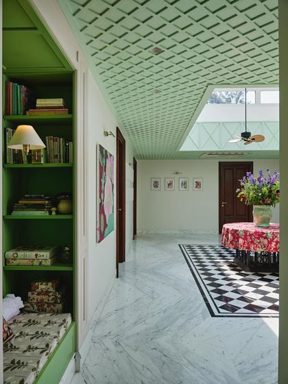 The atrium acts as a central corridor, connecting different parts of the home. Here, you can see the transition from the bold checkered floor to the leafy green reading nook, showcasing the home's playful use of color.