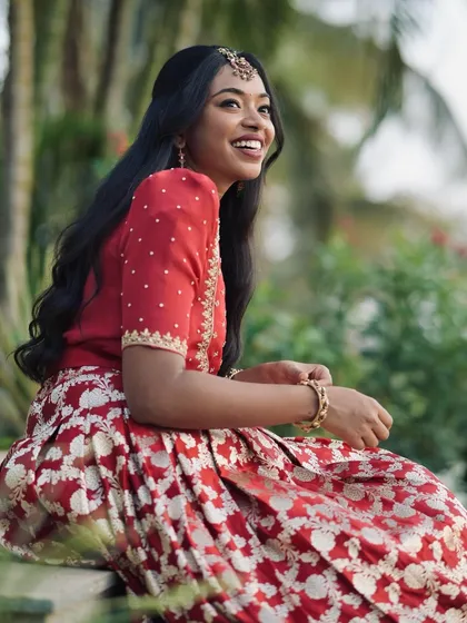 A client looking radiant in a custom cherry red Banarasi lehenga with an intricately embroidered blouse.