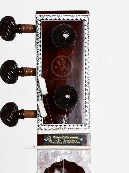 The headstock of an Ustad Vilayat Khan style sitar, showing our maker's mark. The carved pegs are made from rosewood for durability and a good grip.