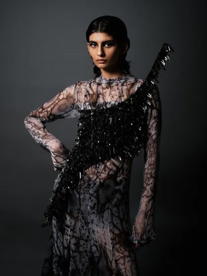 A full-body shot showcasing the complete avant-garde look. The sleek hair and dramatic makeup work together with the textured, abstract dress to create a cohesive and futuristic fashion statement.