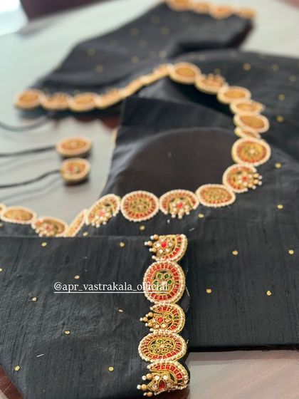 A black blouse with a V-neckline, adorned with circular kemp stone motifs.