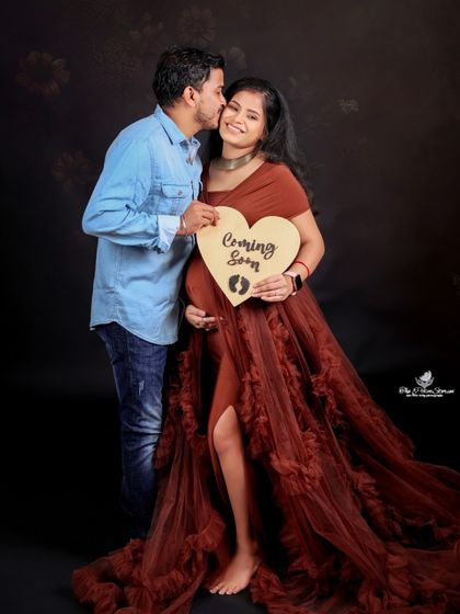 A kiss on the cheek and a "Coming Soon" sign make for a perfect, joyful shot. This pose is a client favorite for its sweetness and clear message.