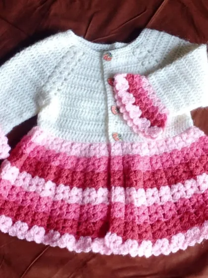 A classic baby frock in shades of pink and white. The gradient stripes are created with a traditional granny stripe stitch, making it a timeless and cozy piece.