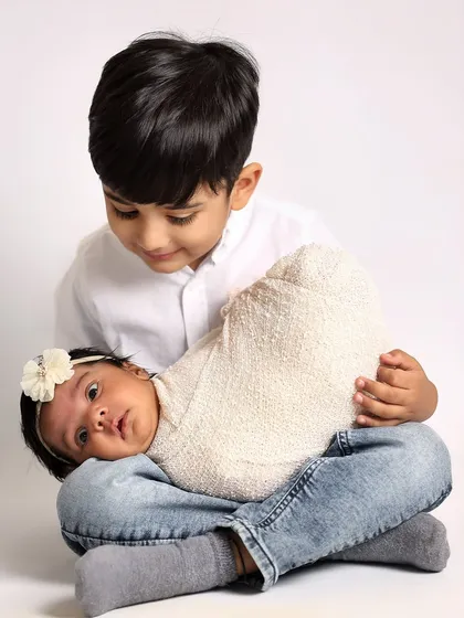 A big brother looks down lovingly at his newborn sister, who is resting on his lap. This pose is wonderful for showing the gentle connection between siblings.