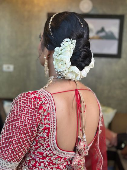 A full and voluminous bridal bun decorated with white roses and baby's breath. This is a timeless wedding hairstyle that pairs beautifully with a traditional red lehenga and gold jewellery.