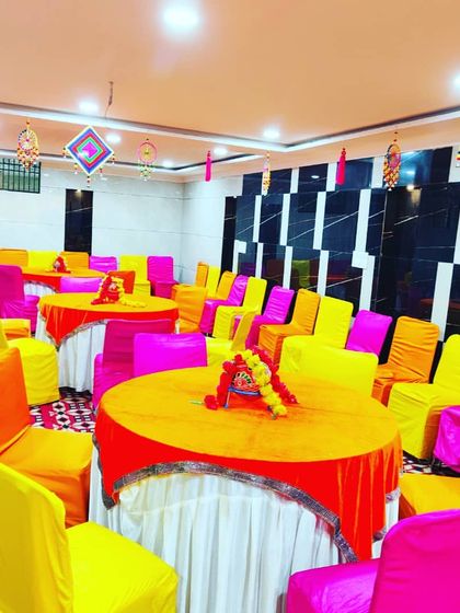 A bright and colourful indoor seating arrangement for a Haldi or Mehendi function, with orange, yellow, and pink chair covers.