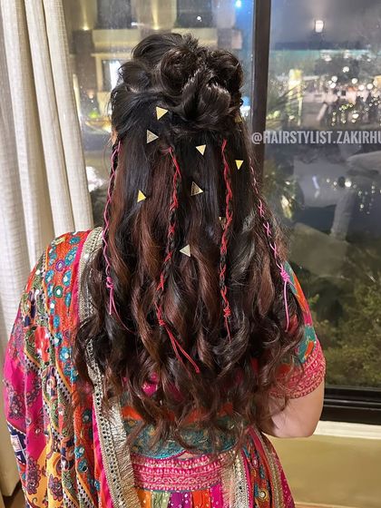 A fun and festive half-up style with a top knot, curls, and colorful thread and gold accessories. Perfect for a vibrant Mehendi or Sangeet.