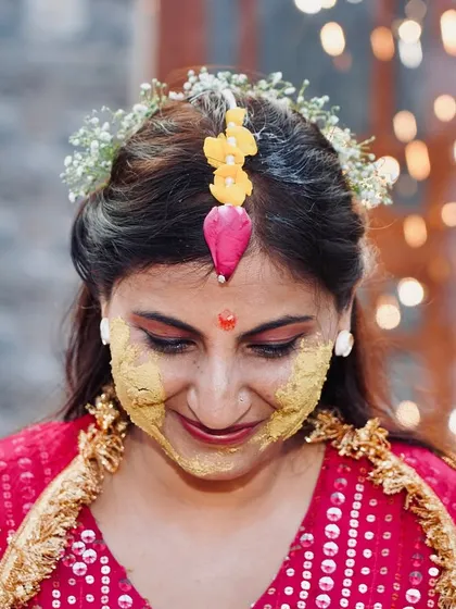 A close up shot of the bride with haldi on her face, wearing a floral maang tikka. This photo highlights the happy and serene expression amidst the fun.