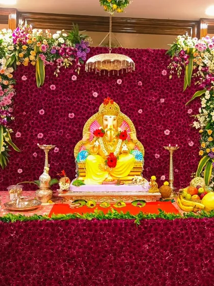 This luxurious design combines a rich, deep red floral base and backdrop with corners of fresh, exotic flowers. The contrast creates a royal and opulent setting for the Ganpati idol.