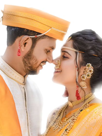 A close-up, candid shot of a Maharashtrian couple sharing a smile. The image highlights the intricate details of their wedding attire, from the bride's nath to the groom's mundavalya.