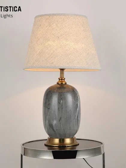 This contemporary lamp features a ceramic base with a grey marble-effect pattern and a simple fabric shade. It includes a dual-lit feature, allowing both the base and the shade to glow for added ambiance.