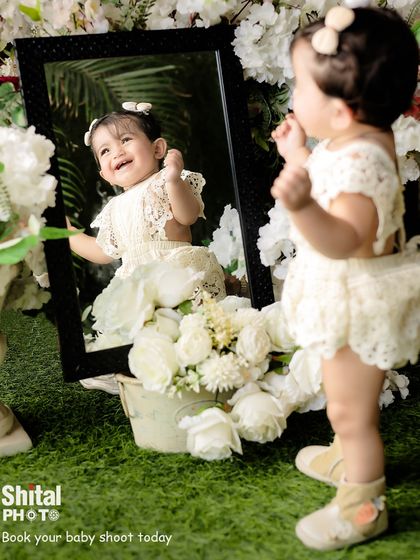 A baby discovers her own reflection in the mirror. Using props like mirrors can lead to wonderful, interactive, and joyful moments during a shoot.