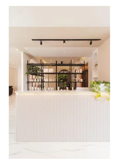 The clean, white reception desk with integrated lighting and fluted details sets a tone of minimalist luxury from the moment a client walks in.