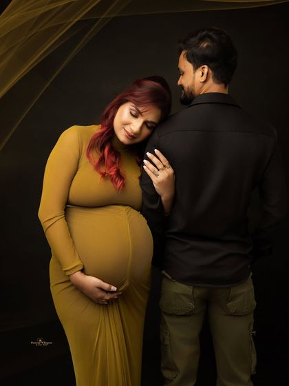 An intimate and modern couple's portrait. The mother-to-be, with her striking red hair, leans gently on her partner, creating a moment of quiet connection.