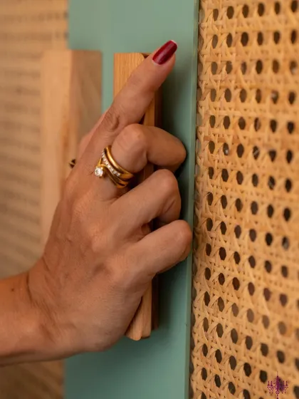 A close-up of a hand on a rattan-paneled wardrobe door, highlighting the use of sustainable materials.