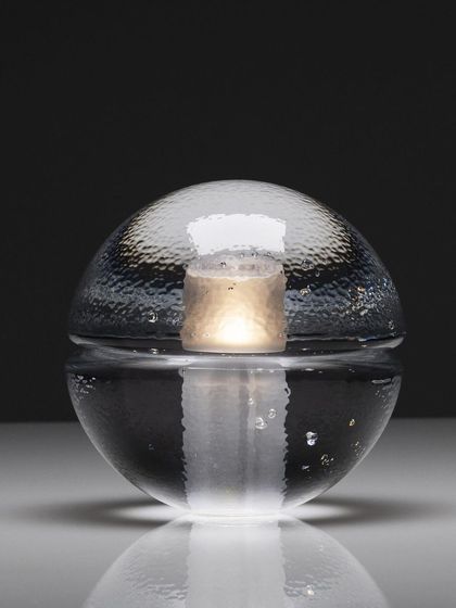 A studio shot of the clear glass 14p, its internal light source creating a beautiful, watery reflection on the surface below.