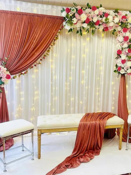 I love playing with unique color combinations, like the warm rust drapes paired with soft pink and white flowers in this setup. The asymmetrical floral arch adds a modern touch, while the fairy lights in the background give it a magical glow. This is a great option for a chic and stylish pre-wedding event.
