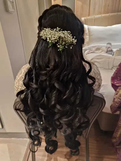 A romantic half-up hairstyle with voluminous, structured curls perfect for an engagement or sangeet. The look is finished with a sprig of fresh baby's breath, adding a touch of softness and elegance.
