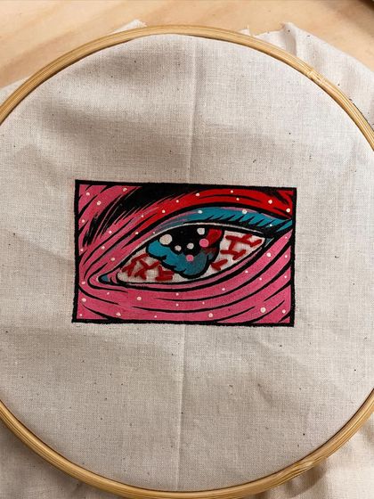 The embroidered eye detail on the back pocket of the pillow, stretched on a hoop.
