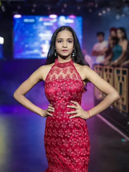 A powerful, hands-on-hips pose from a model in a red gown at 'Walk in Style', showcasing her confidence and the dress's intricate lace detail.