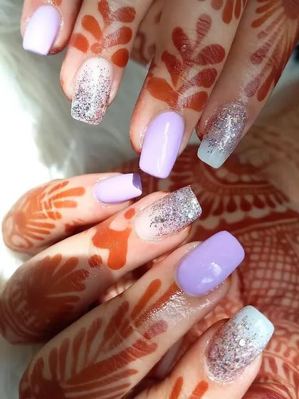 A beautiful combination of pastel lavender and blue-toned glitter nails, shown against a henna-adorned hand.