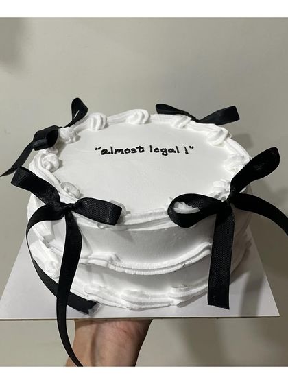 The trendy "bow cake" design. This minimalist white cake is adorned with elegant black ribbons, perfect for a chic "almost legal" 18th birthday celebration.