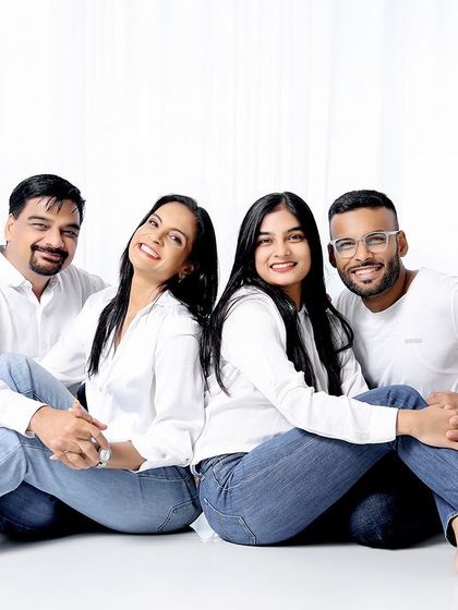 A modern and relaxed portrait of a family with two grown children. The back-to-back pose in matching white shirts and jeans creates a stylish and connected image.