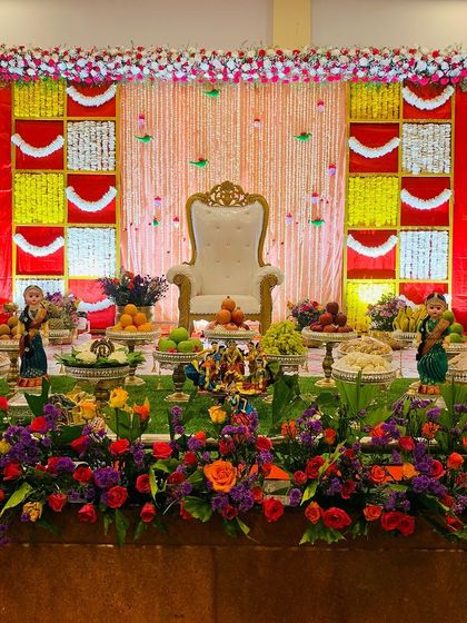 A vibrant and colorful stage for a baby shower. The backdrop uses red, yellow, and white panels, with a full floral arrangement in the foreground creating a festive and joyful atmosphere.