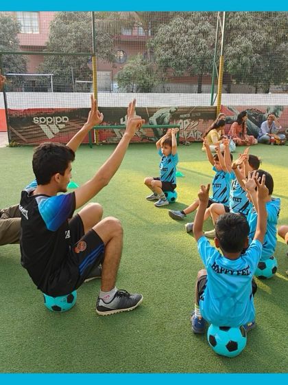 Hands up if you’re having fun! Our coaches lead by example, joining the kids in warm up exercises and stretches. Here, they are all sitting on their footballs, which is a fun way to improve balance.