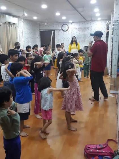 An instructor guides a large group of children through a Taekwondo warm-up exercise. This wide shot shows the full class learning basic stances and movements together in our spacious studio.