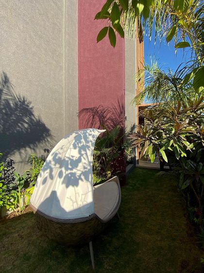 A cozy, private court designed as a green oasis. The unique boat-like outdoor furniture provides a comfortable spot for relaxation, surrounded by lush tropical plants that create a sense of enclosure and escape.