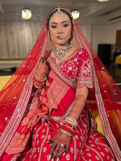 Kritika in her stunning red bridal lehenga, veiled and ready for her ceremony. The makeup is regal and elegant, with a focus on her expressive eyes.