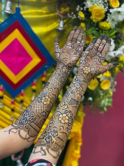 The bride showing off her floral henna against a colorful mehendi backdrop. The design looks so vibrant and festive.