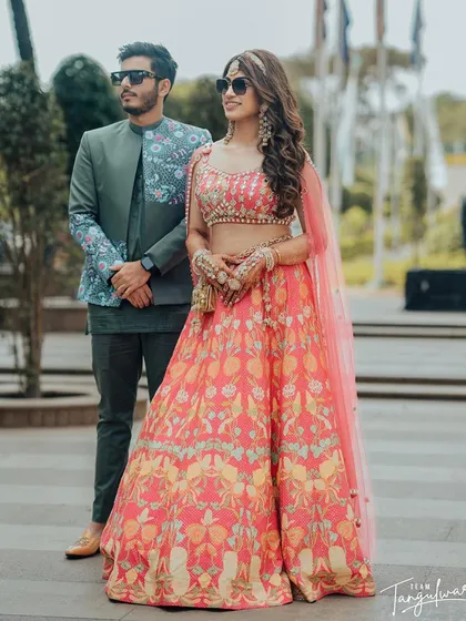 A Mehendi bride with her groom, her hair styled in voluminous waves with a statement headband.