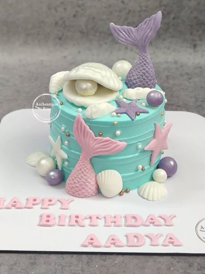 A beautiful mermaid cake with pink and purple mermaid tails, seashells, and pearls.