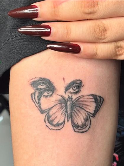 A surrealist butterfly tattoo where the wings are made of eyes. A unique and artistic fine-line piece for the thigh.