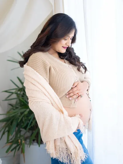A cozy and intimate portrait by the window. The mom-to-be, in a knit sweater and jeans, cradles her bump, creating a warm and personal image.