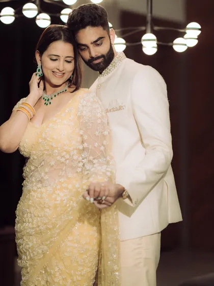 A classic, elegant portrait from an indoor engagement shoot. The couple holds hands, their pose exuding confidence and grace under the soft glow of a contemporary light fixture.