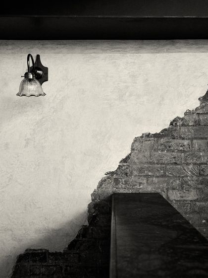 The simple form of a wall lamp against the rough texture of the exposed brick and plaster wall.