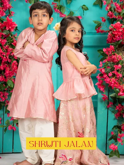 A classic brother-sister duo in blush pink is always a heartwarming sight. Here, the boy's simple Angrakha style kurta and the girl's peplum top with a floral embroidered skirt create a perfectly coordinated look that’s both elegant and adorable for any family function.