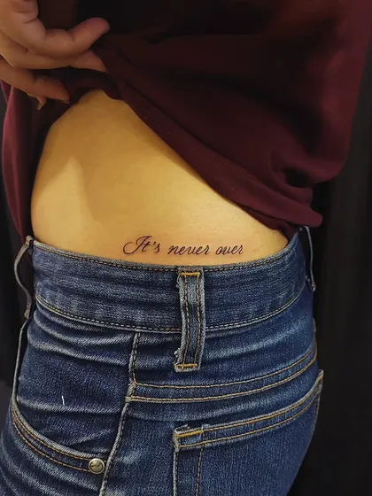 "It's never over" inked on the hip. The cursive script and placement make this a personal and empowering message.