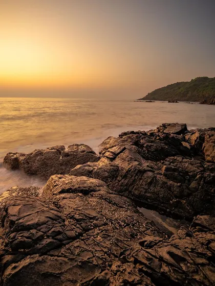 The textures of the rocks on the shoreline are highlighted by the warm, golden light of sunset. This is a classic example of capturing the magic of golden hour by the sea.
